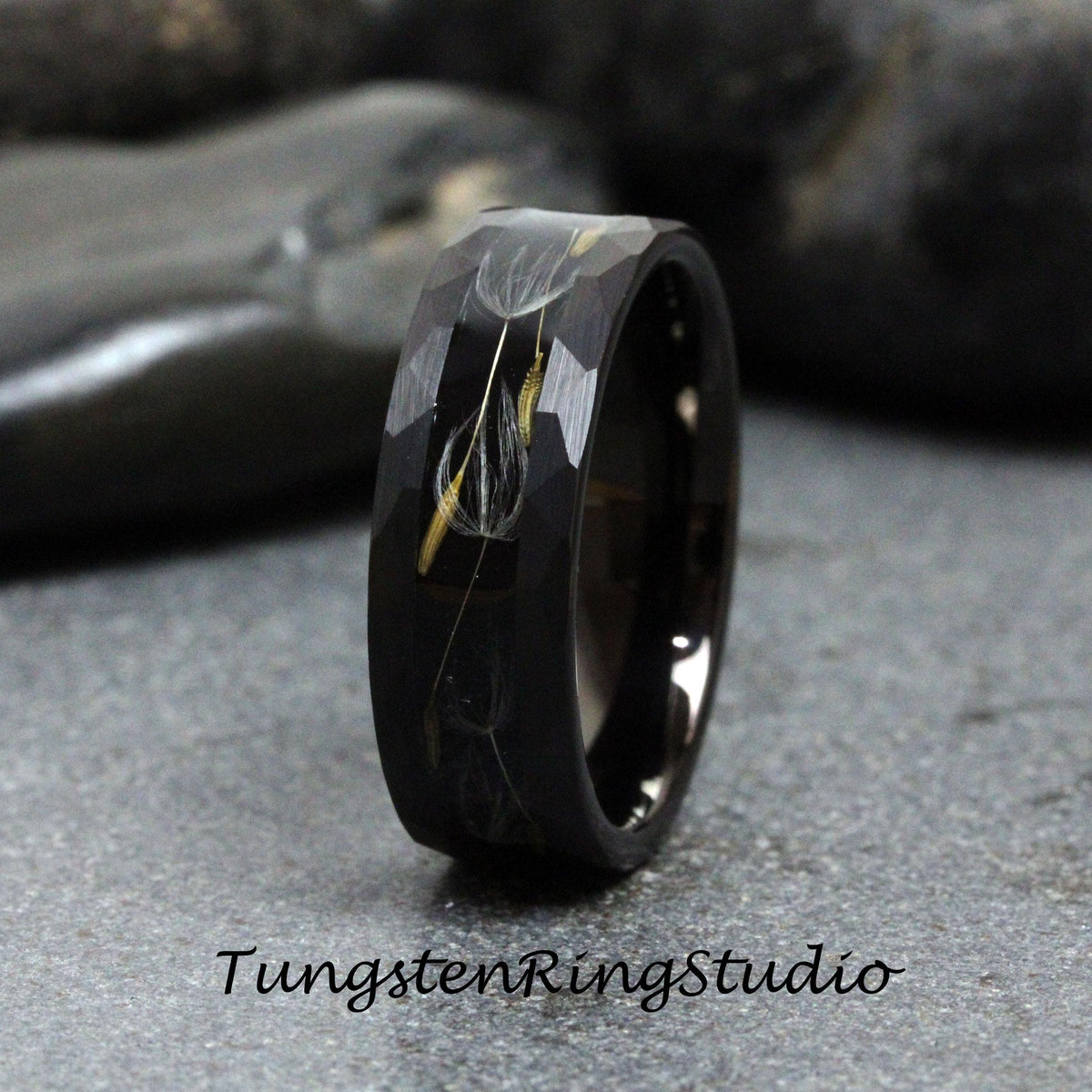 May include: A black tungsten carbide ring with a brushed finish and a design of dandelion seeds embedded in the band.
