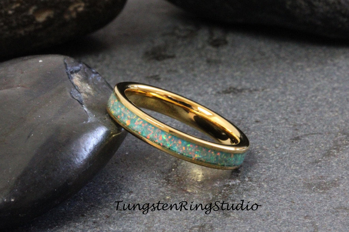 May include: A gold tungsten ring with a thin band of green opal inlay. The ring is shown on a gray background.