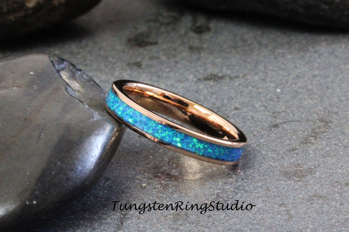 May include: A rose gold tungsten ring with a blue opal inlay. The ring is on a gray background.