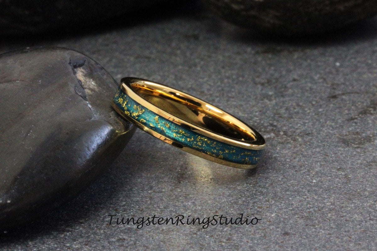 May include: A gold tungsten carbide ring with a green and gold inlay. The ring has a polished finish and is set on a dark gray background.