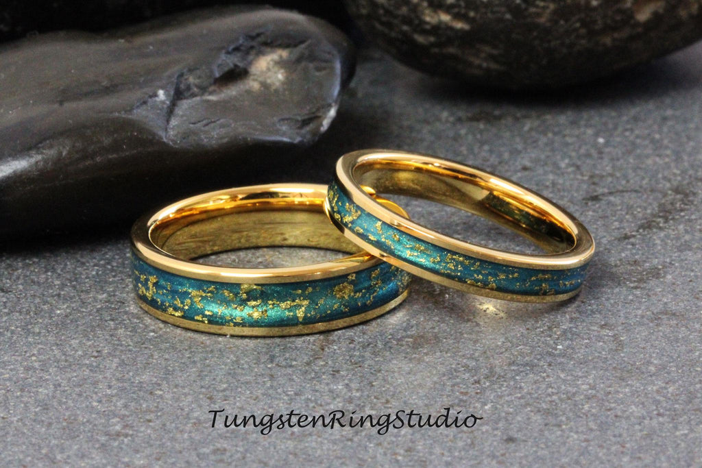 May include: Two gold wedding bands with a teal blue and gold inlay. The bands are on a dark gray background.