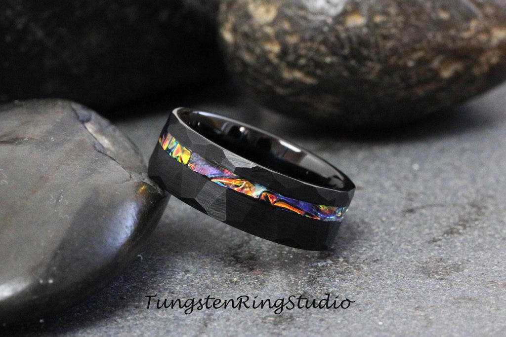 May include: Black tungsten carbide ring with a hammered finish and a colorful inlay. The inlay features a variety of colors, including blue, green, and orange.