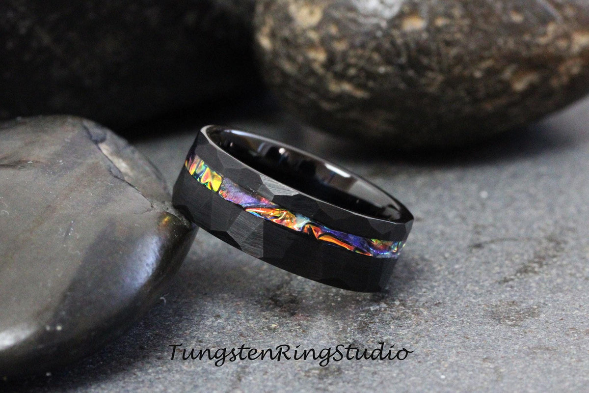 May include: Black tungsten carbide ring with a hammered finish and a colorful inlay. The inlay features a variety of colors, including blue, green, and orange.