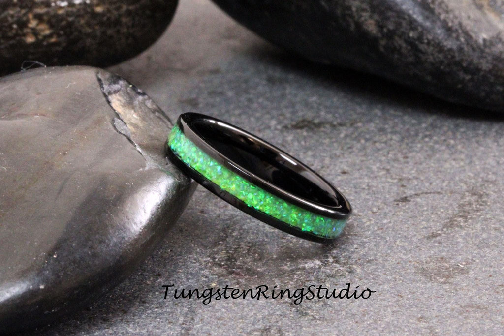 May include: A black tungsten ring with a green opal inlay. The ring is on a gray stone surface.