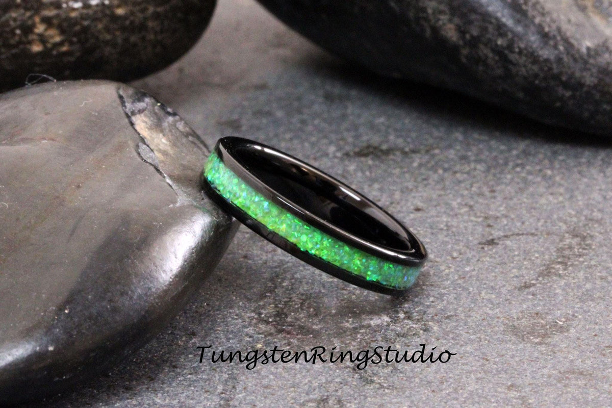 May include: A black tungsten ring with a green opal inlay. The ring is on a gray stone surface.