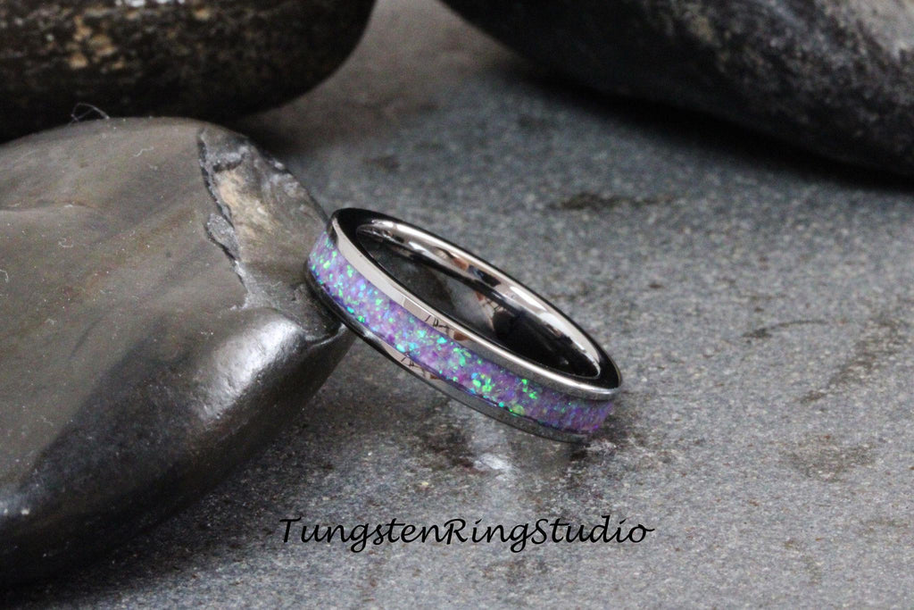May include: A silver tungsten ring with a purple and green opal inlay. The ring is on a gray stone background.