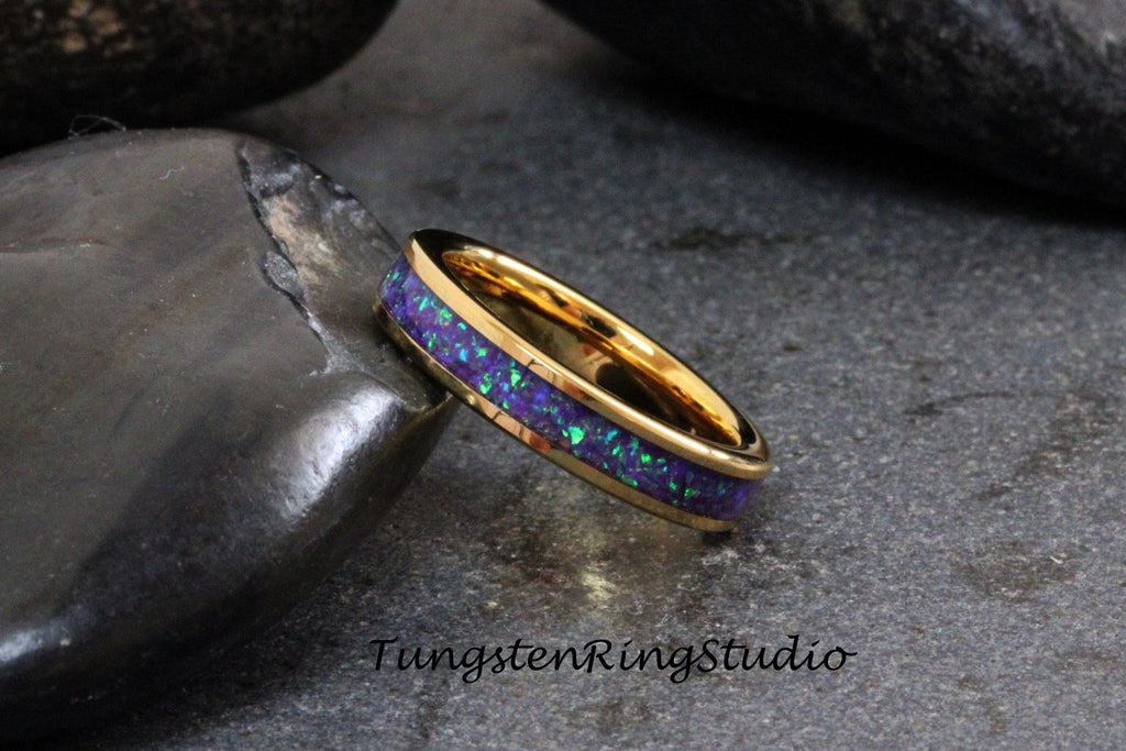 May include: A gold tungsten carbide ring with a purple and green opal inlay. The ring is on a dark gray background.