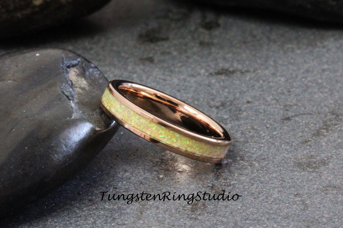May include: A rose gold tungsten carbide ring with a thin band of white opal inlay. TungstenRingStudio is printed below the ring.
