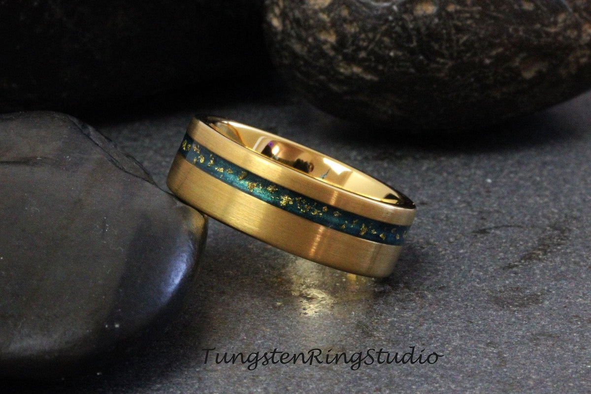 May include: A gold tungsten carbide ring with a green and gold inlay. The ring has a brushed finish and a beveled edge.