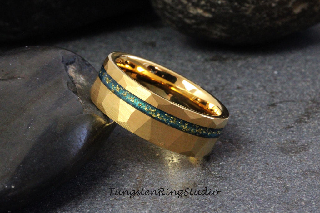 May include: A gold tungsten carbide ring with a blue and gold inlay. The ring has a hammered finish and a beveled edge.