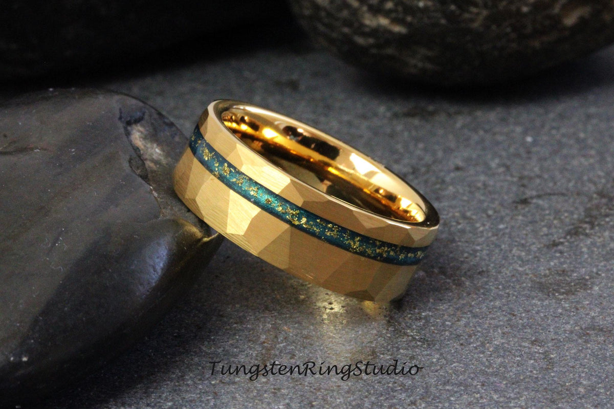 May include: A gold tungsten carbide ring with a blue and gold inlay. The ring has a hammered finish and a beveled edge.