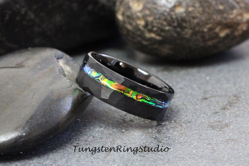 May include: Black tungsten ring with a hammered finish and a thin iridescent abalone inlay. The ring is shown on a dark gray background.