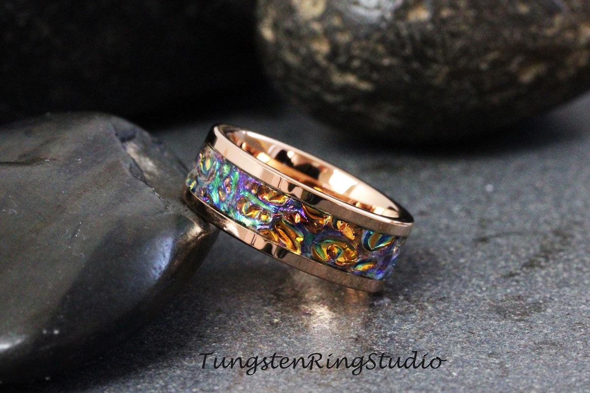 May include: A rose gold tungsten carbide ring with a colorful, iridescent inlay. The inlay has a swirling pattern of blue, green, and gold.