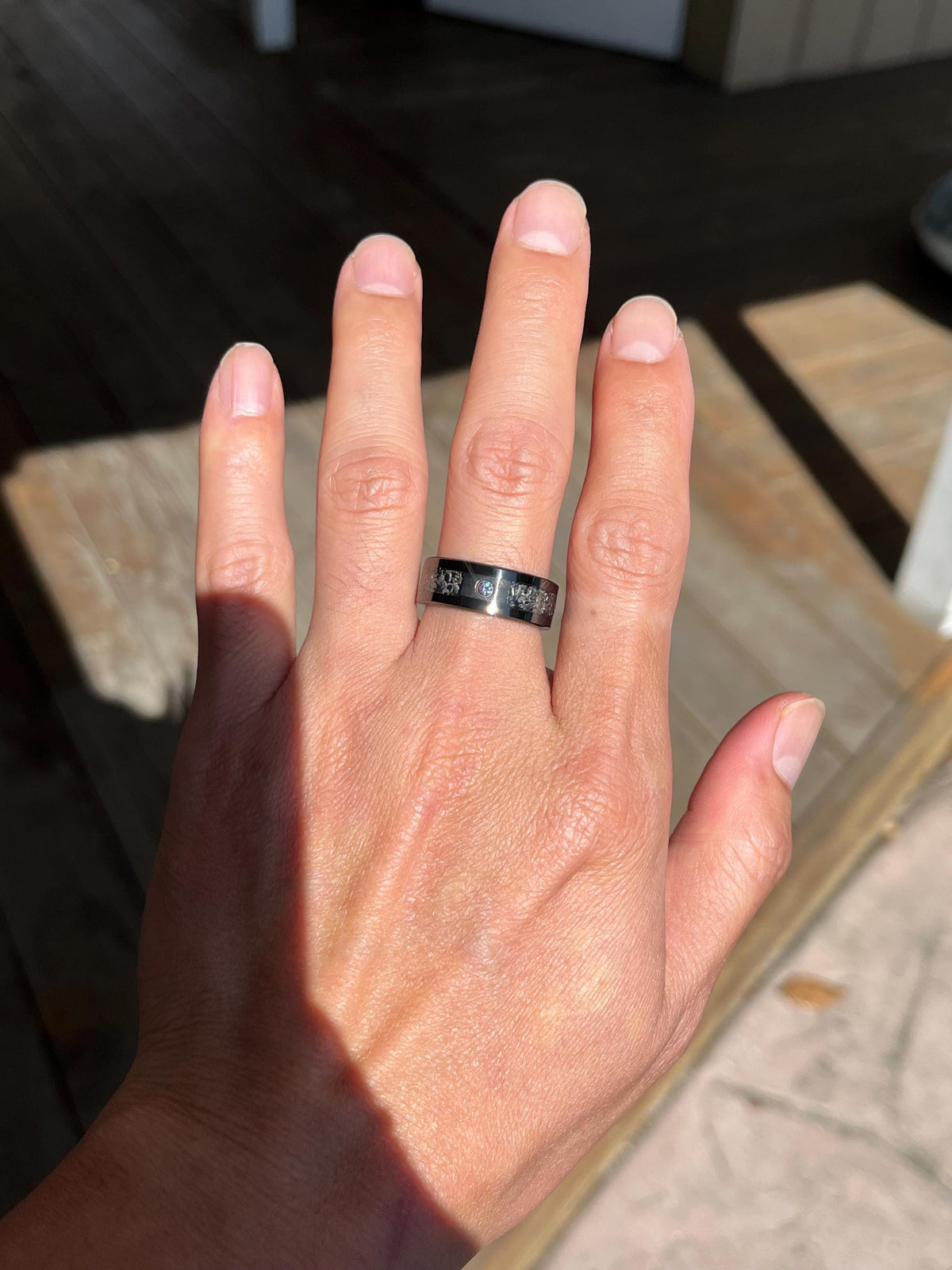 May include: A silver-toned metal band ring featuring a flat, polished surface with a central row of small, circular, clear inset stones. The ring has a wide, uniform width and a reflective finish, displaying a series of evenly spaced decorative accents.