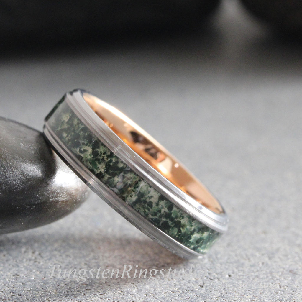 May include: A ring featuring a dark grey metallic outer band with a central inlay of mottled green stone and a smooth rose gold interior. The band has a polished finish and a distinct stepped edge design, showcasing a textured green mineral pattern.