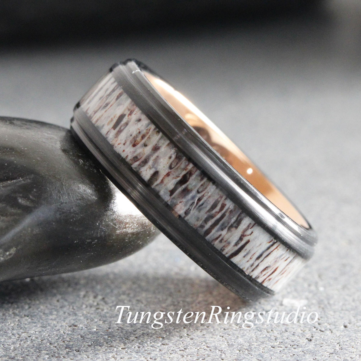 May include: A ring featuring a black metal band with a central inlay of textured, white and brown organic material. The interior of the band is a polished rose gold color. The text TungstenRingstudio is visible at the bottom of the image.