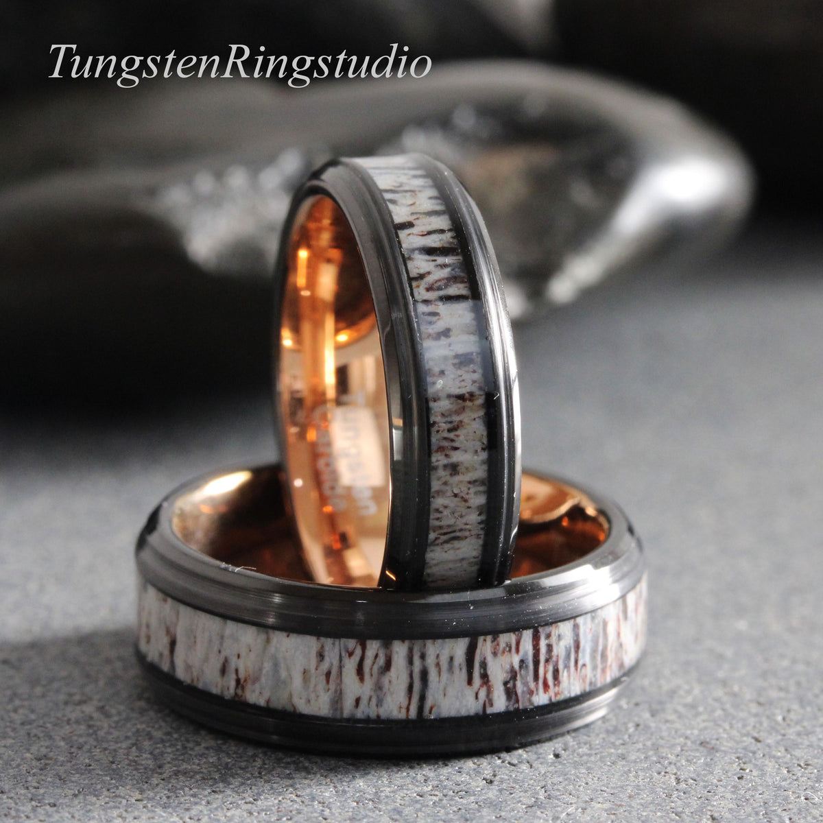 May include: Two rings featuring a black metal band with a central inlay of textured, light-colored antler material. The interior of each ring has a polished rose gold finish. The text TungstenRingstudio is visible in the upper left corner.