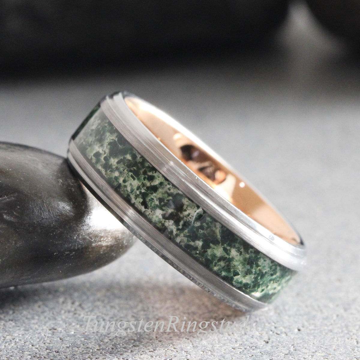 May include: A silver-toned metal ring featuring a wide, textured inlay of dark green and black mottled stone. The interior of the band has a smooth, polished rose gold-colored finish. The outer edges of the ring are raised and have a brushed metallic texture.